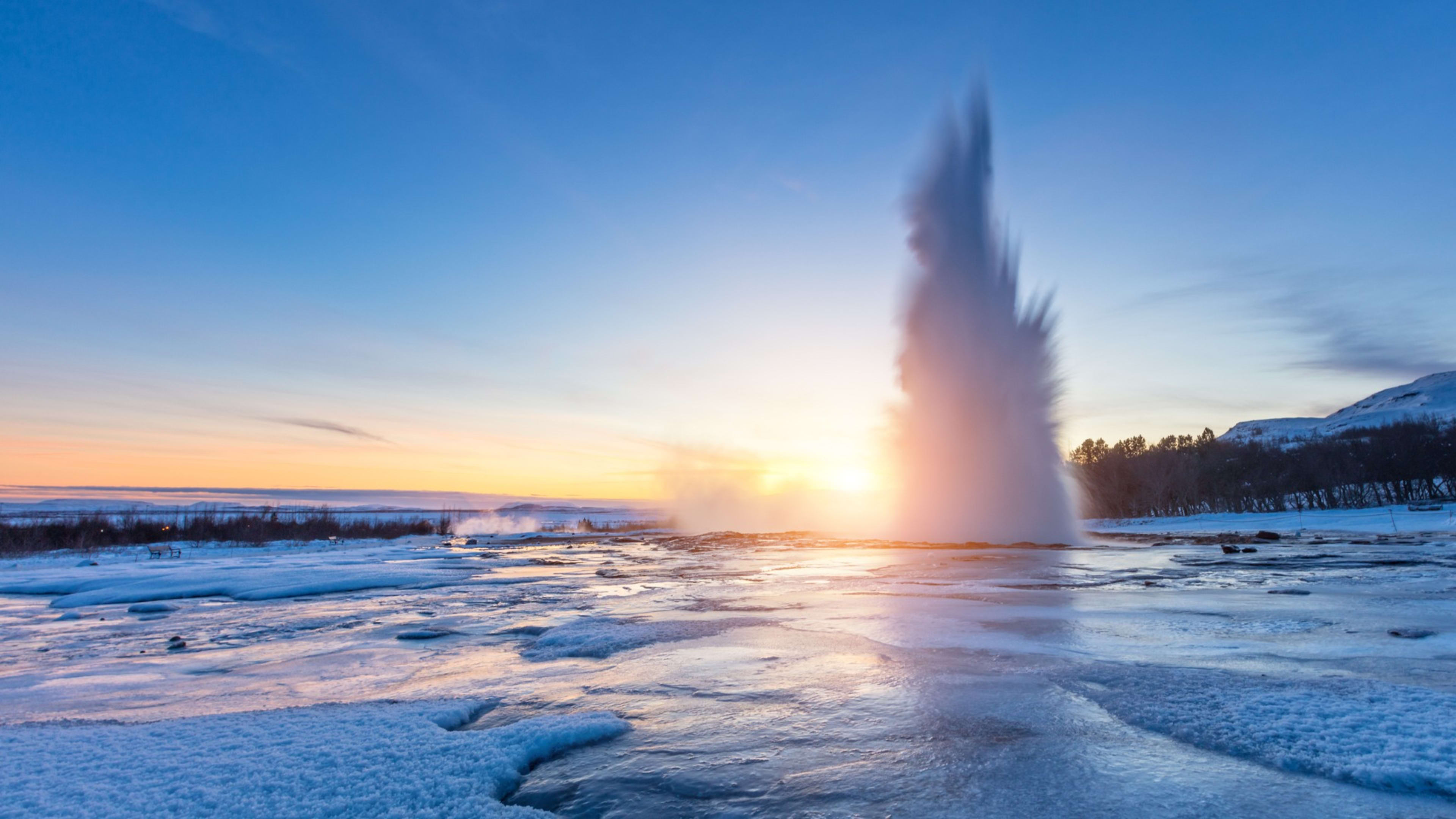 The Strokkur geyser erupting in winter against a sunset