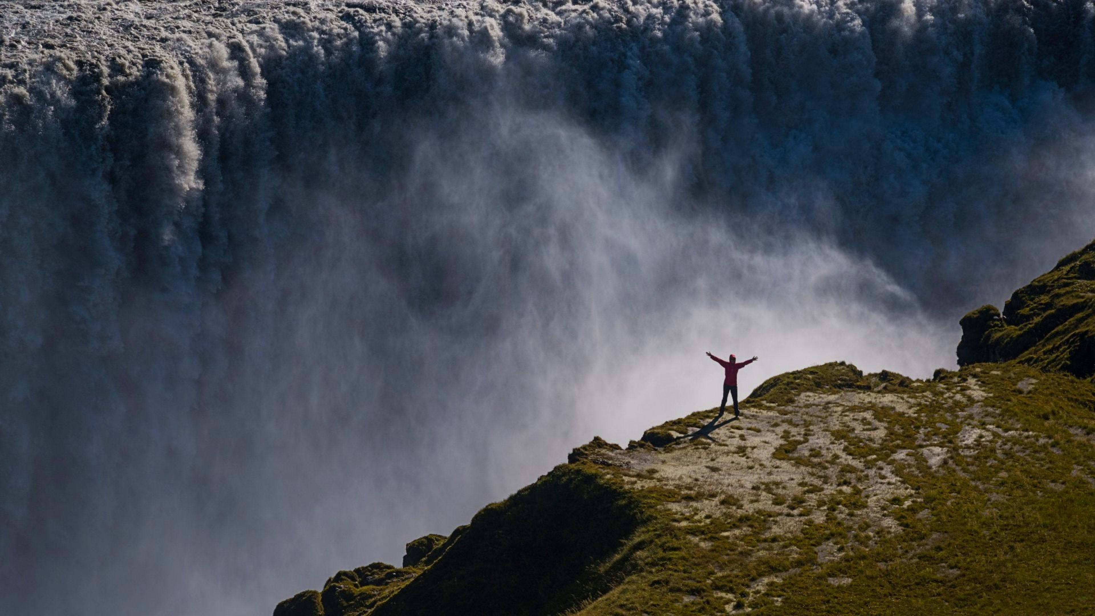 A man standing in front of the Dettifoss waterfall