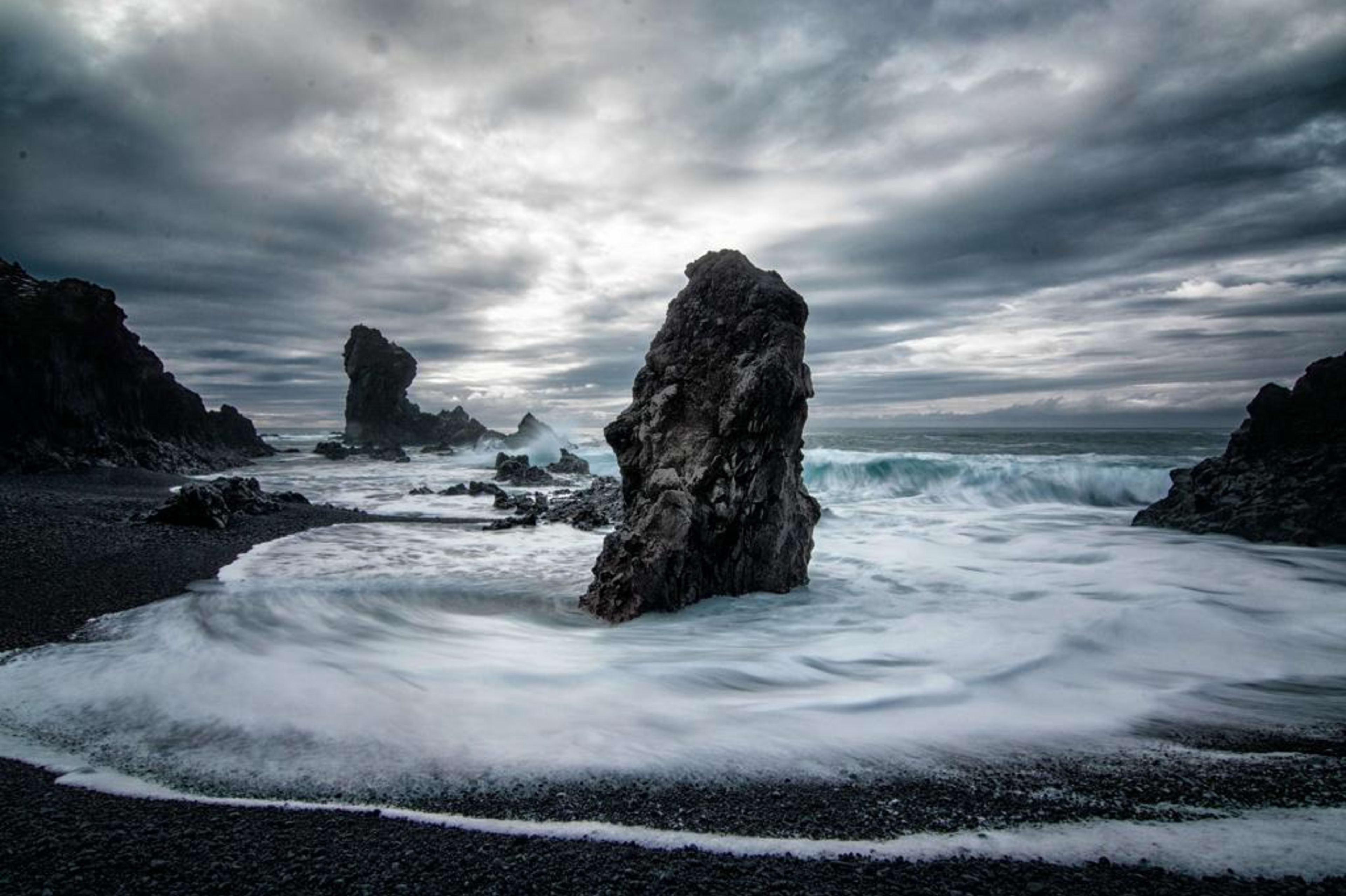 Towering volcanic rock formations surrounded by crashing Atlantic waves on the black sand beach of Djúpalónssandur, Snæfellsnes Peninsula, Iceland.