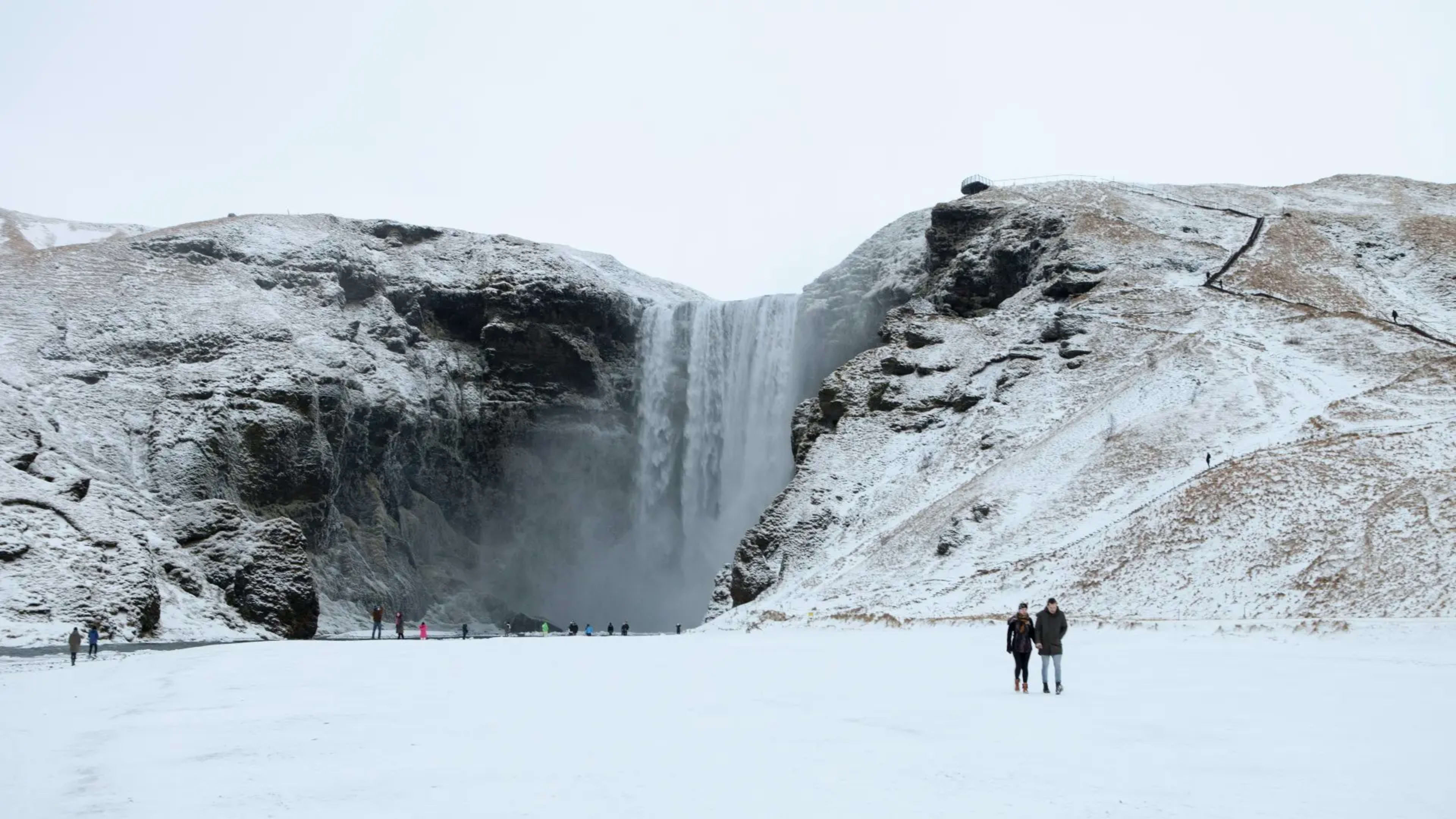 Couple walking by a snow covered Skógafoss waterfall