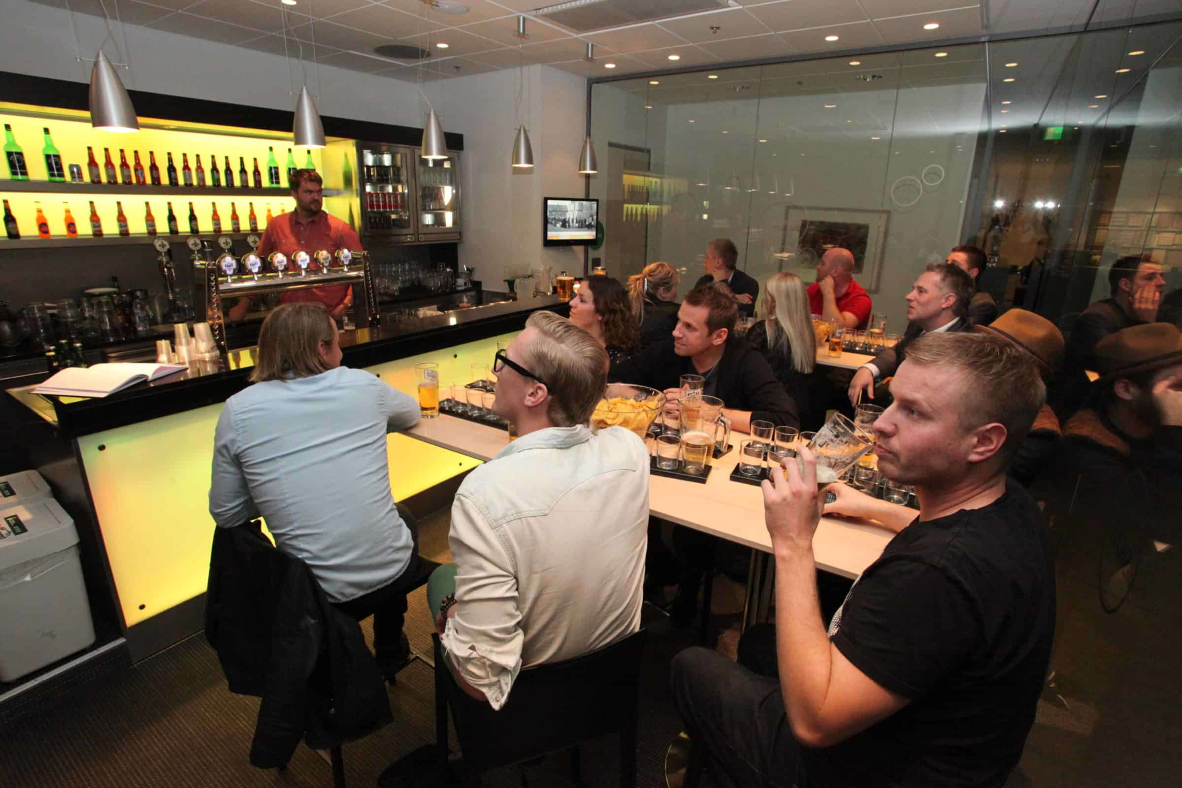 group of people seated with beer flights listening to an expert behind a bar