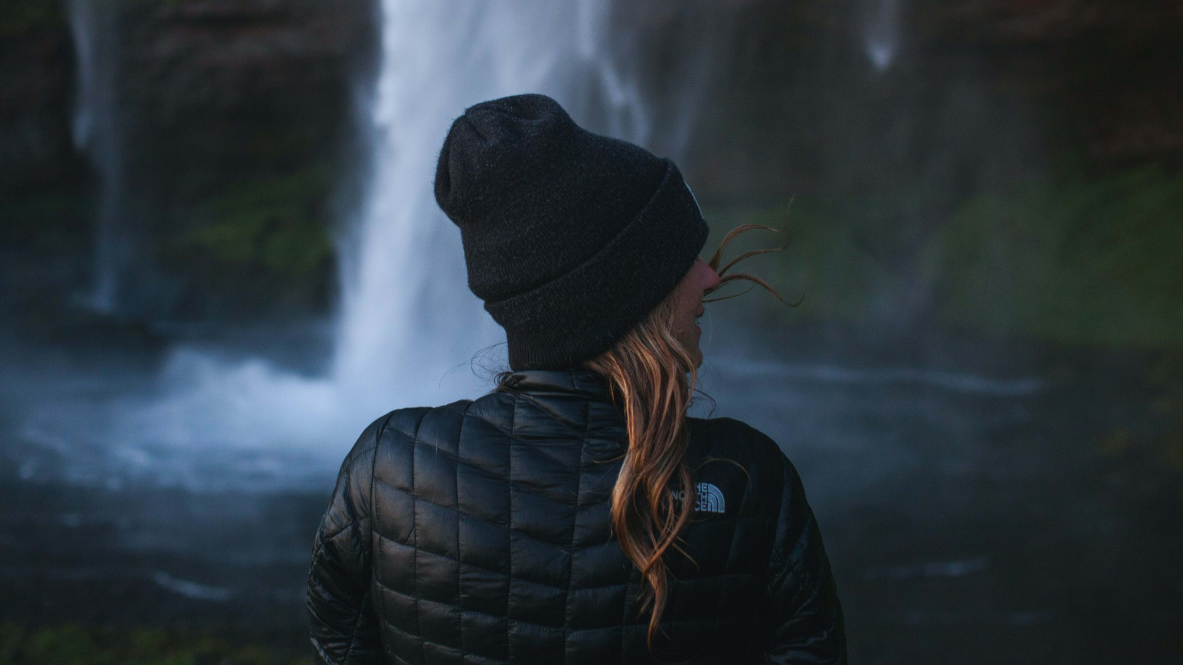 A woman with a beanie standing in front of a waterfall in Iceland
