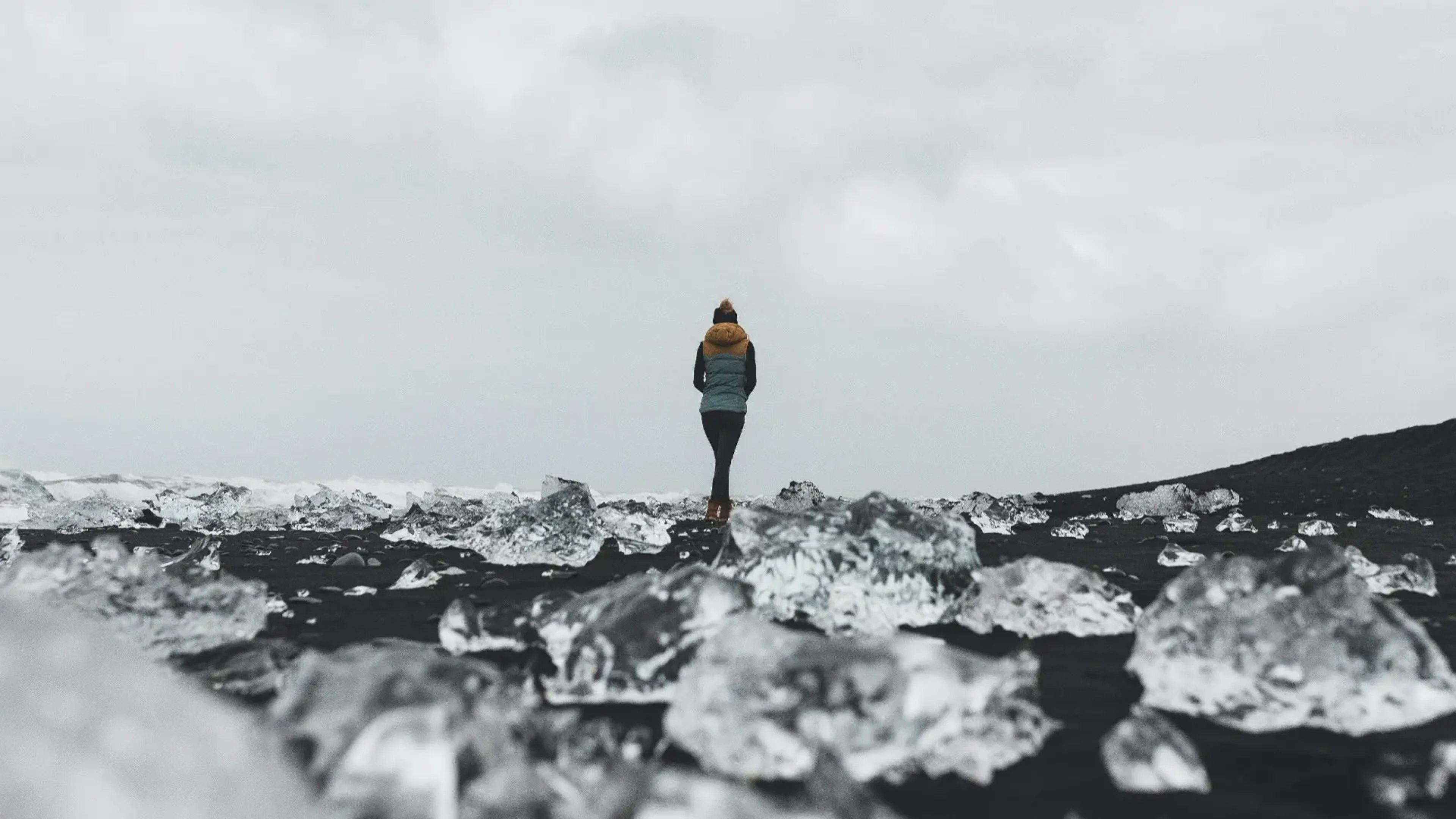 woman walking alone through chunks of ice on black sand beach