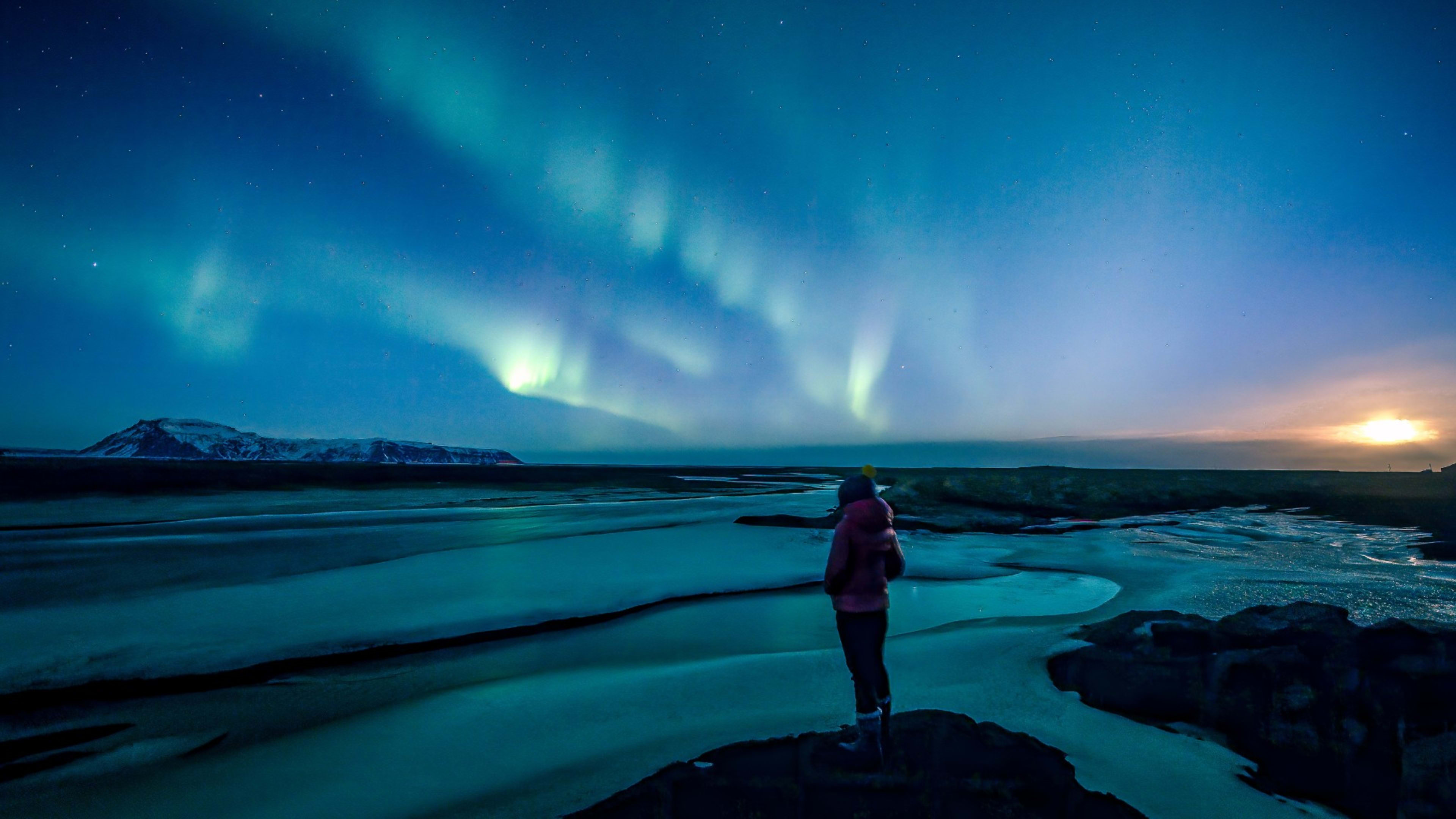 A woman watching the Northern Lights on the edge of a lake