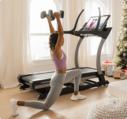 Woman off of their treadmill following her iFIT trainer with dumbbell weights in hand.