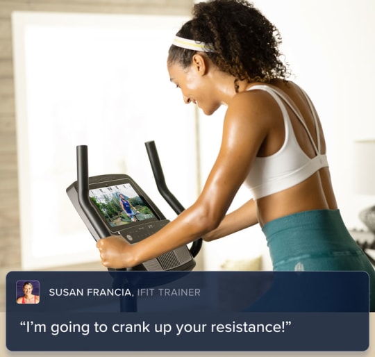 Woman biking on the machine. and looking at her iFIT trainer all from the comfort of a room in her home.