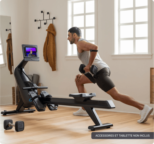 Man is watching iFIT trainer and adjusting the display of his rower while stood up.