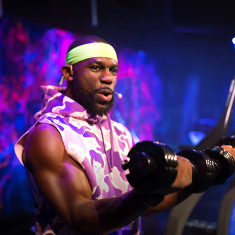 Coach curling dumbbells in a studio class setting.