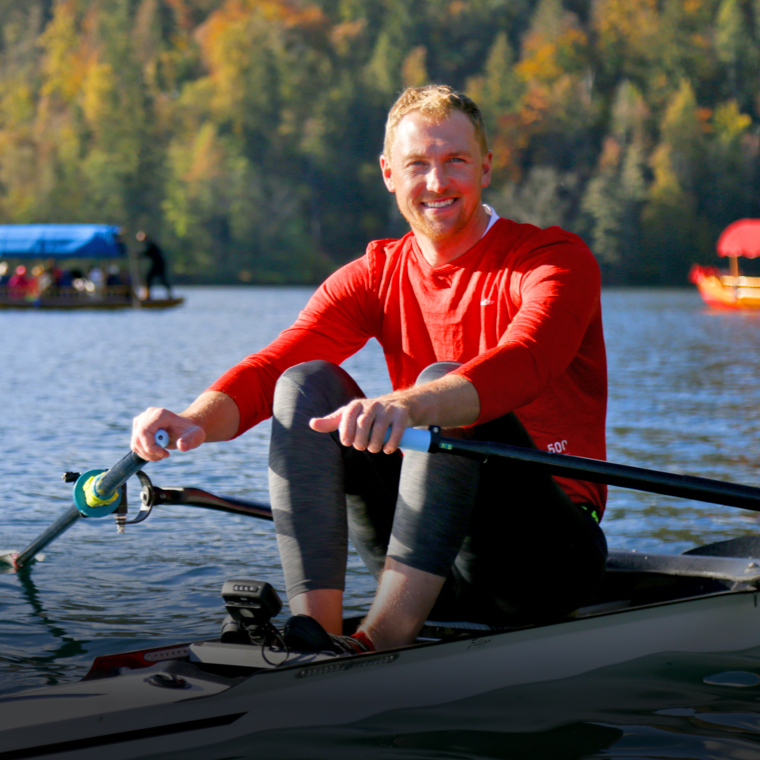 Alex Gregory smiling at the camera and rowing