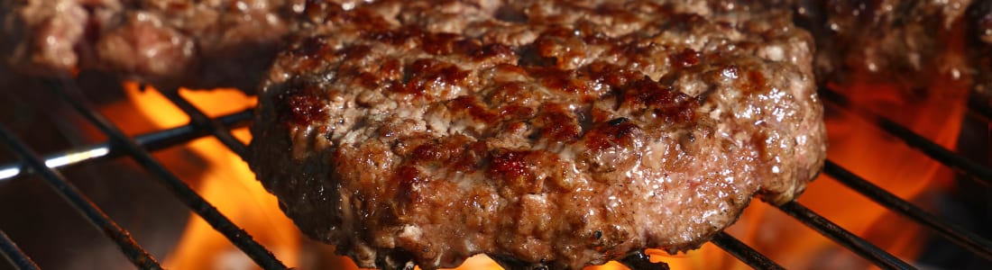 Hamburger patty being grilled on an open flame barbecue