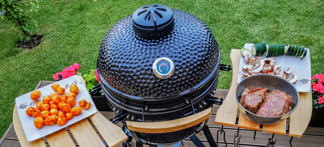 Kamado grill on a patio, with food and accessories