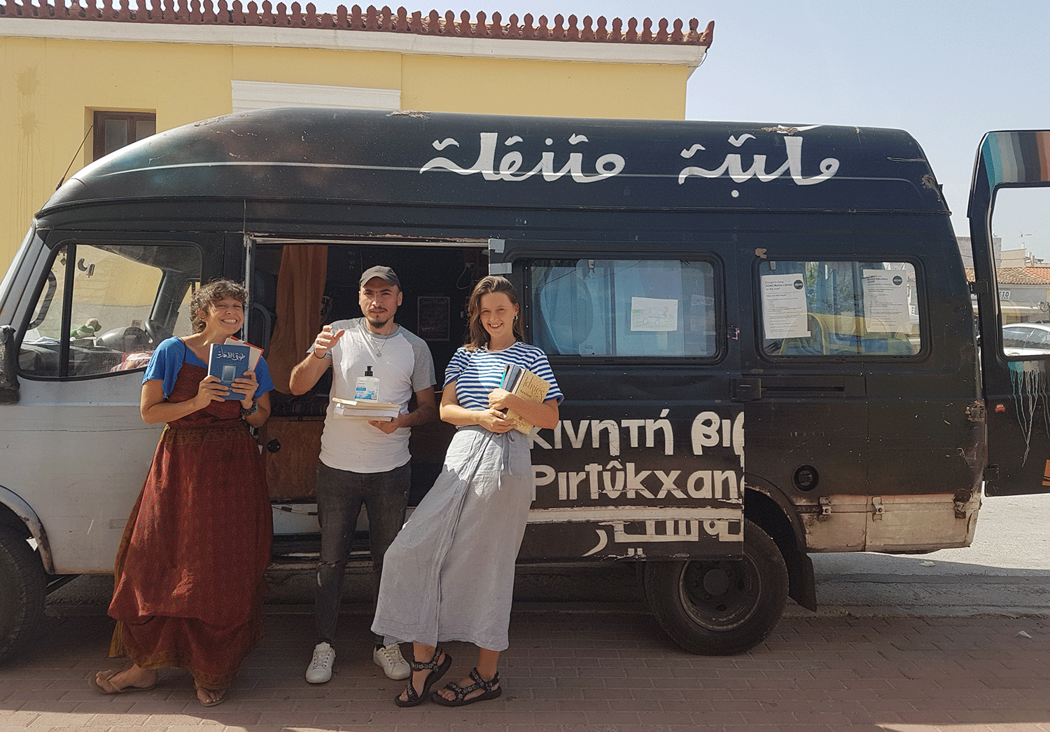 Becka, an ECHO Coordinator, left, poses with volunteer Abo Jaafar from Raqqa, Syria; and Keira, a fellow Coordinator; in front of the mobile library.