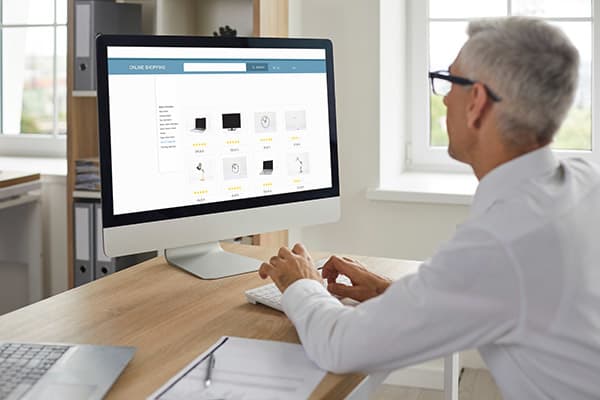 Man shopping online. Senior businessman sitting at work desk, looking at computer display, browsing Internet gadget outlet, buying new office equipment, adding items to cart