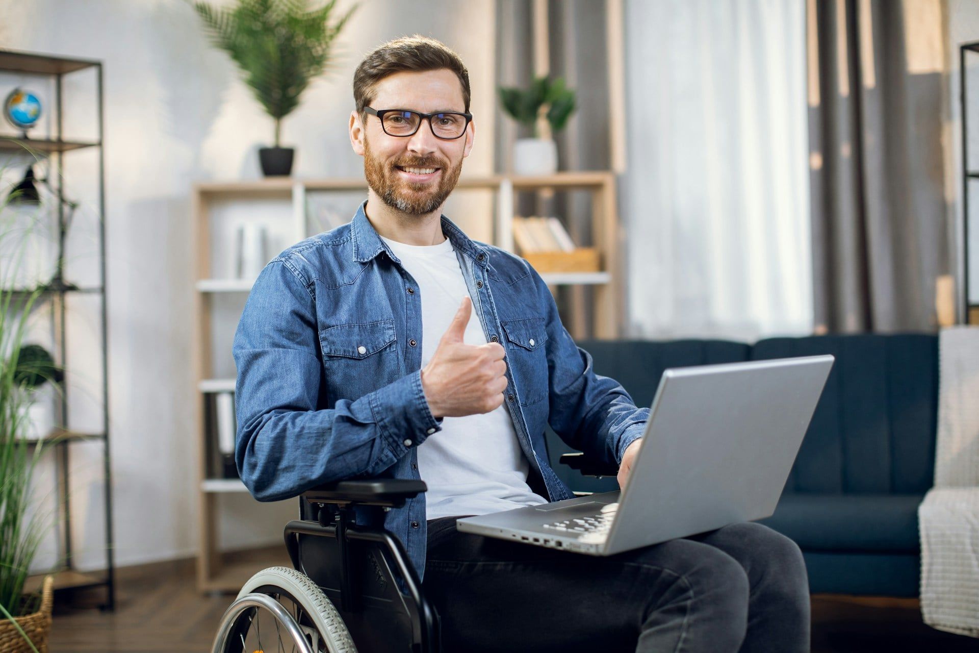 A man smiles in a wheelchair giving a thumb’s up with a laptop on his lap