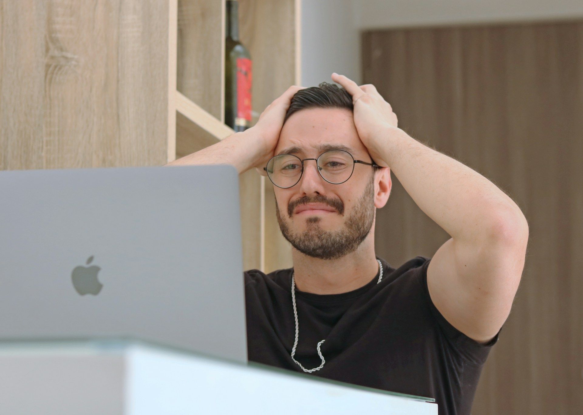 A man looks stressed with his hands on his head while working at a laptop