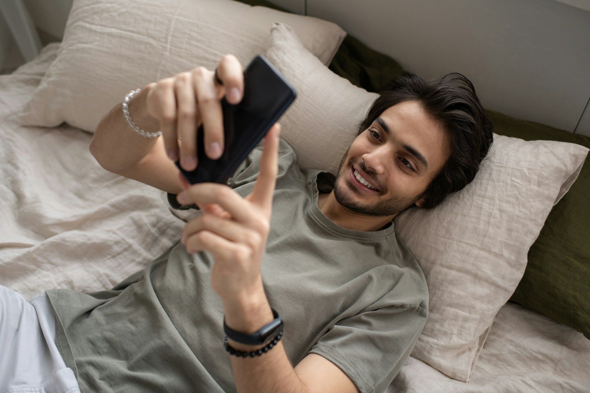 A man lying down in bed, relaxing, using his smartphone to browse websites