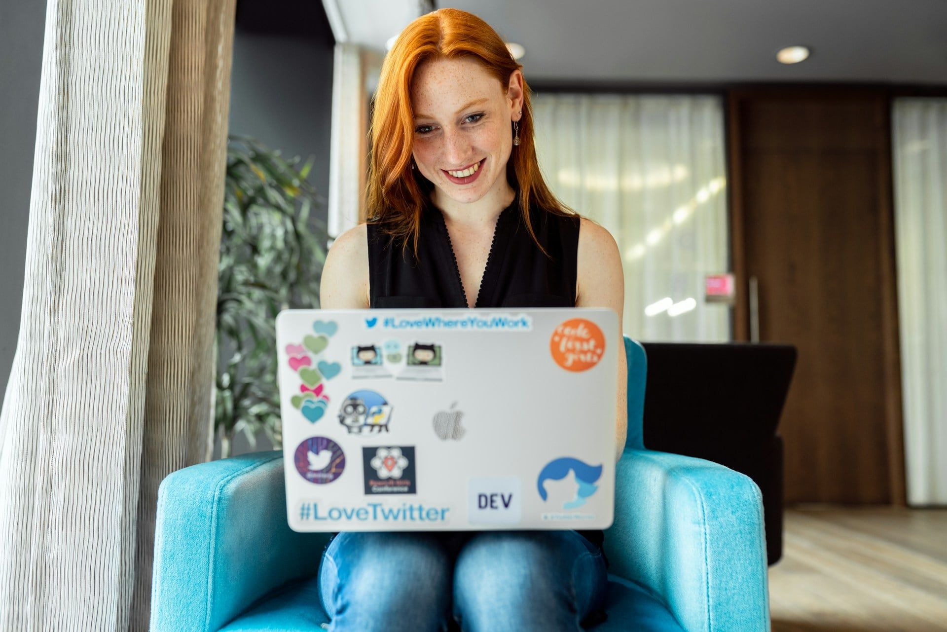 A red-haired woman smiling while she codes a website on her laptop