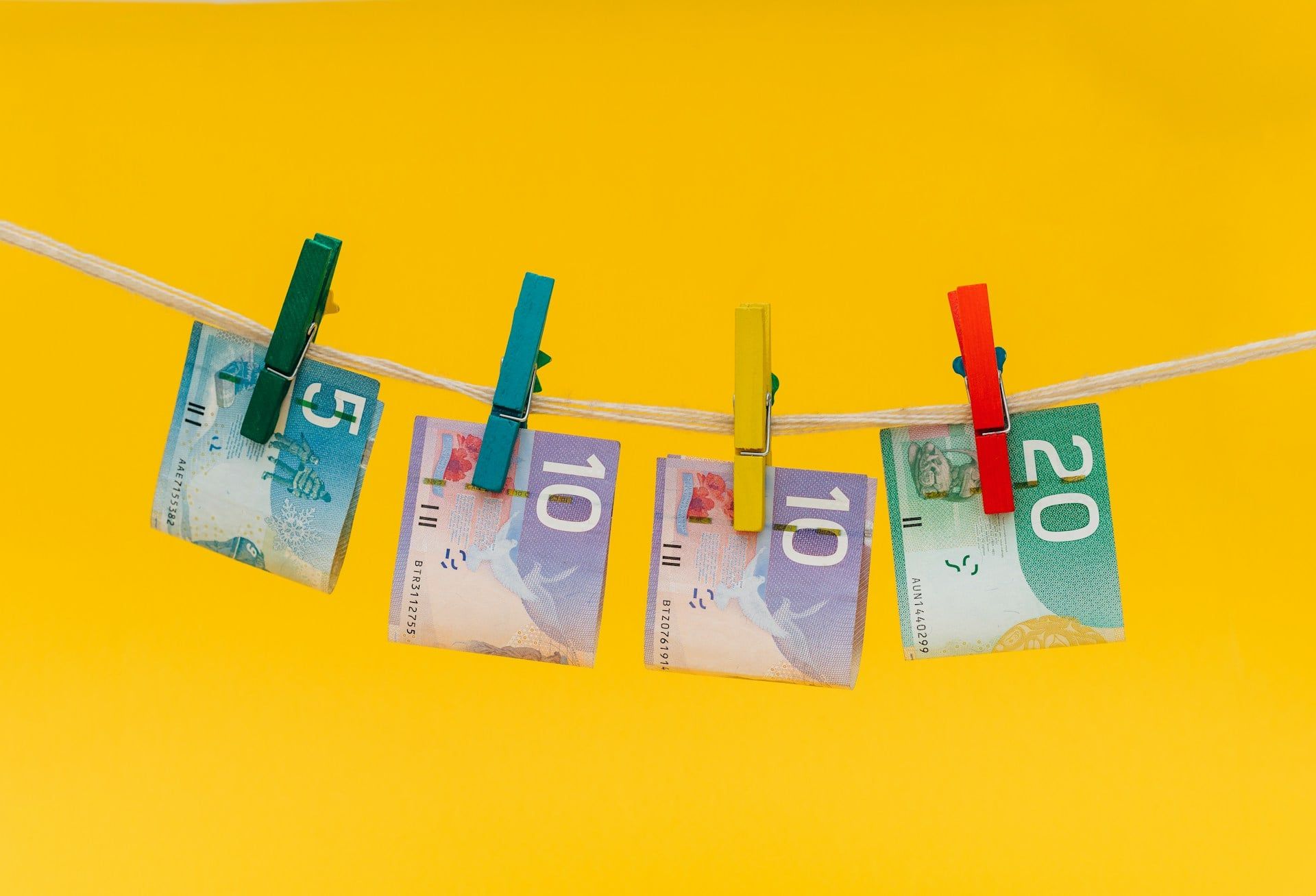 An aesthetic yellow background with a few Canadian dollars pegged on a piece of string