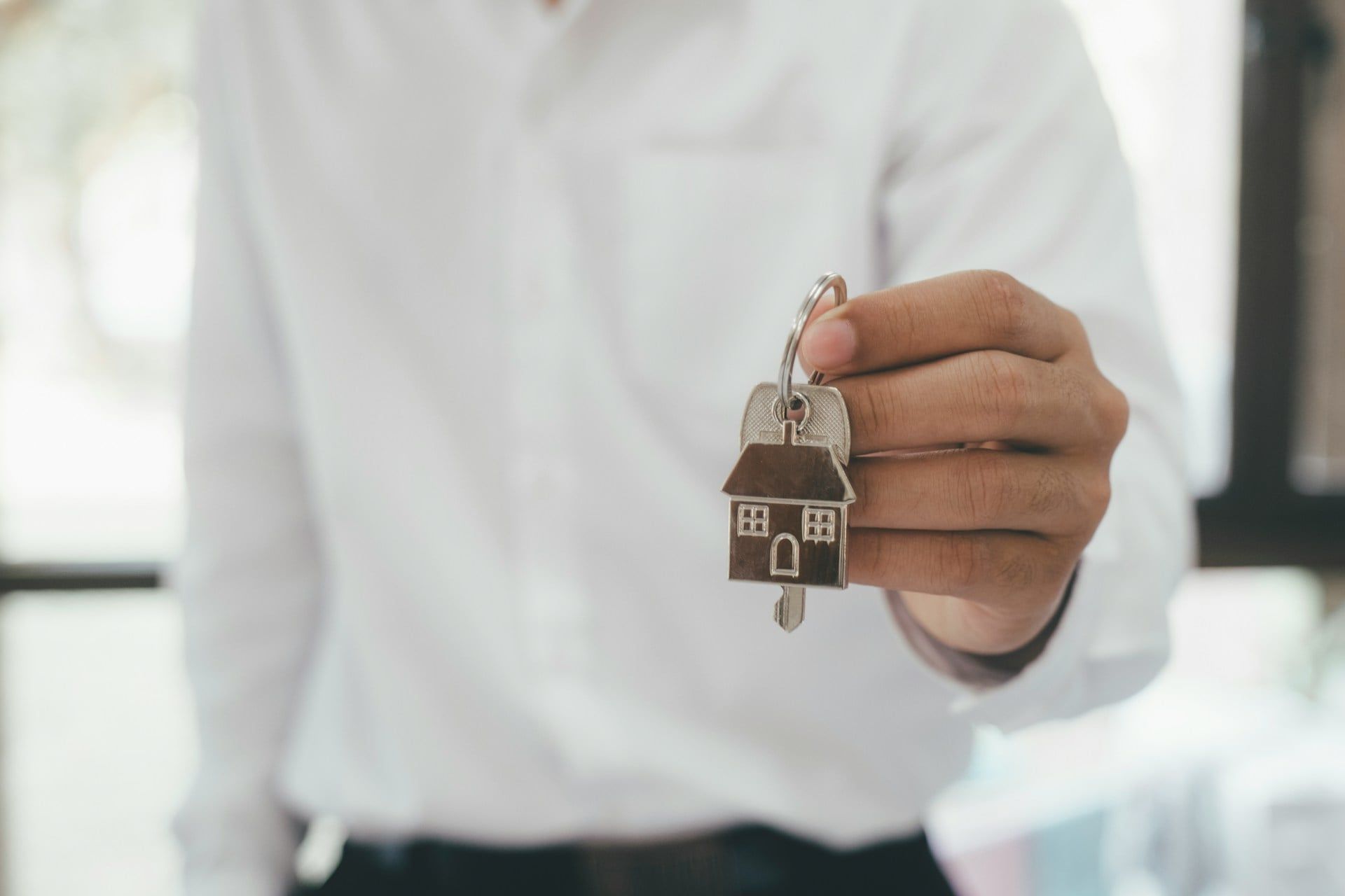 A real estate agent holding out a set of keys with a little house keyring attached