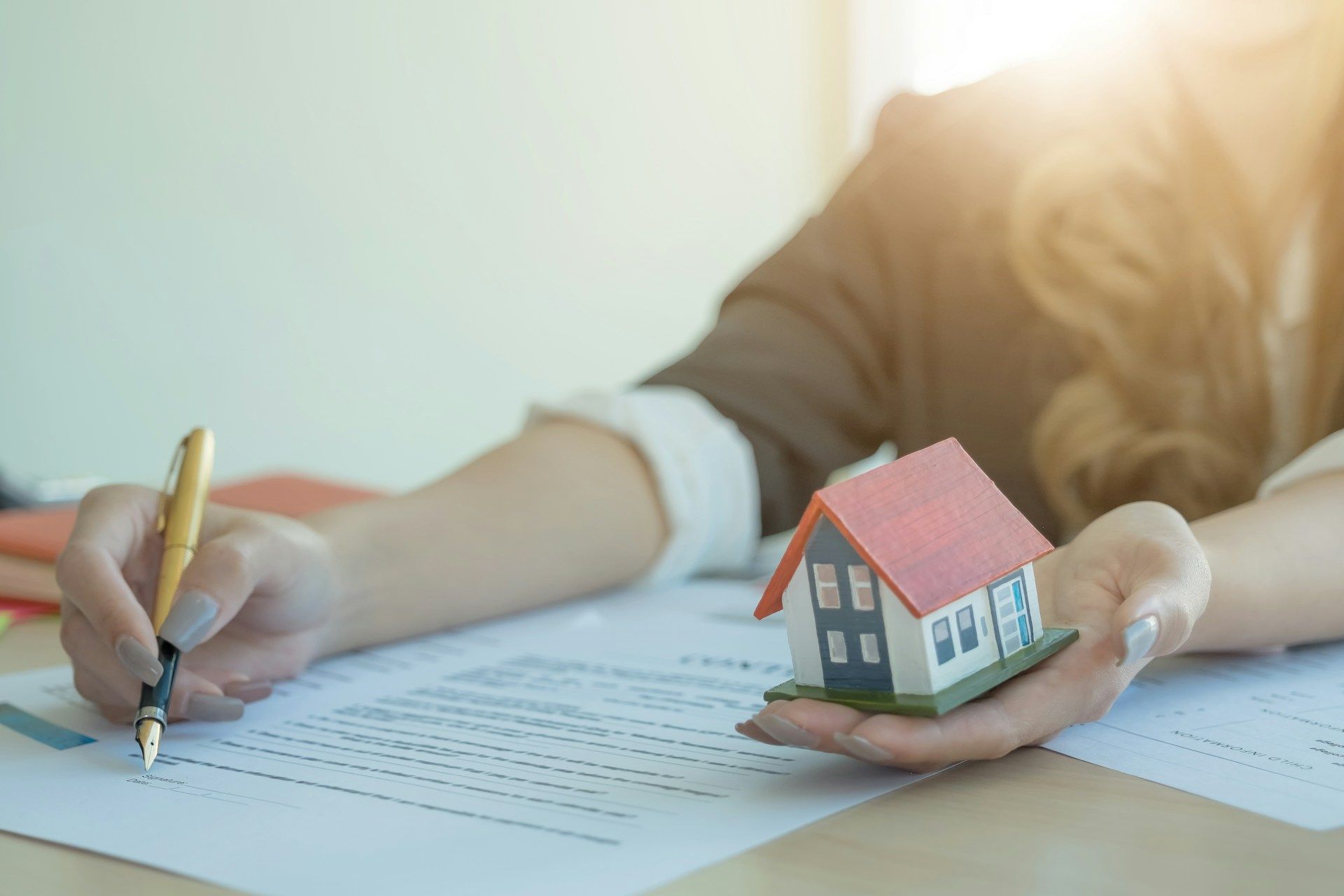  A new home buyer signing a contract while holding a model of a house in their other hand