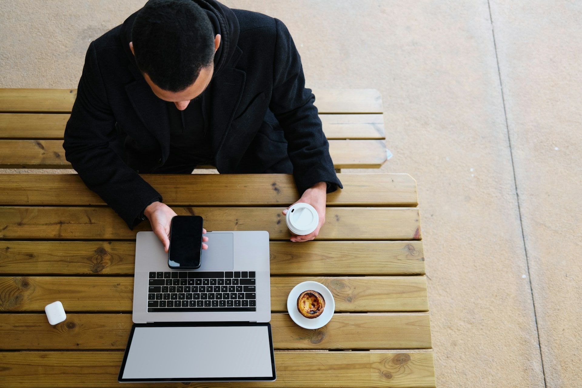 A top-down view of someone using their laptop at a cafe with their smartphone out