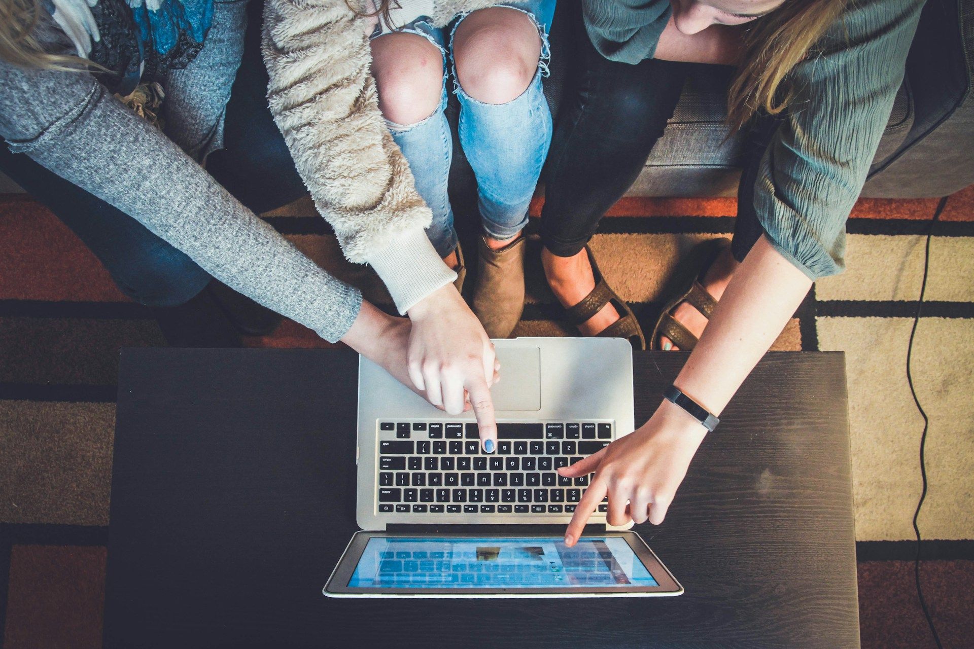 Three people sitting around a laptop all pointing at something on the screen