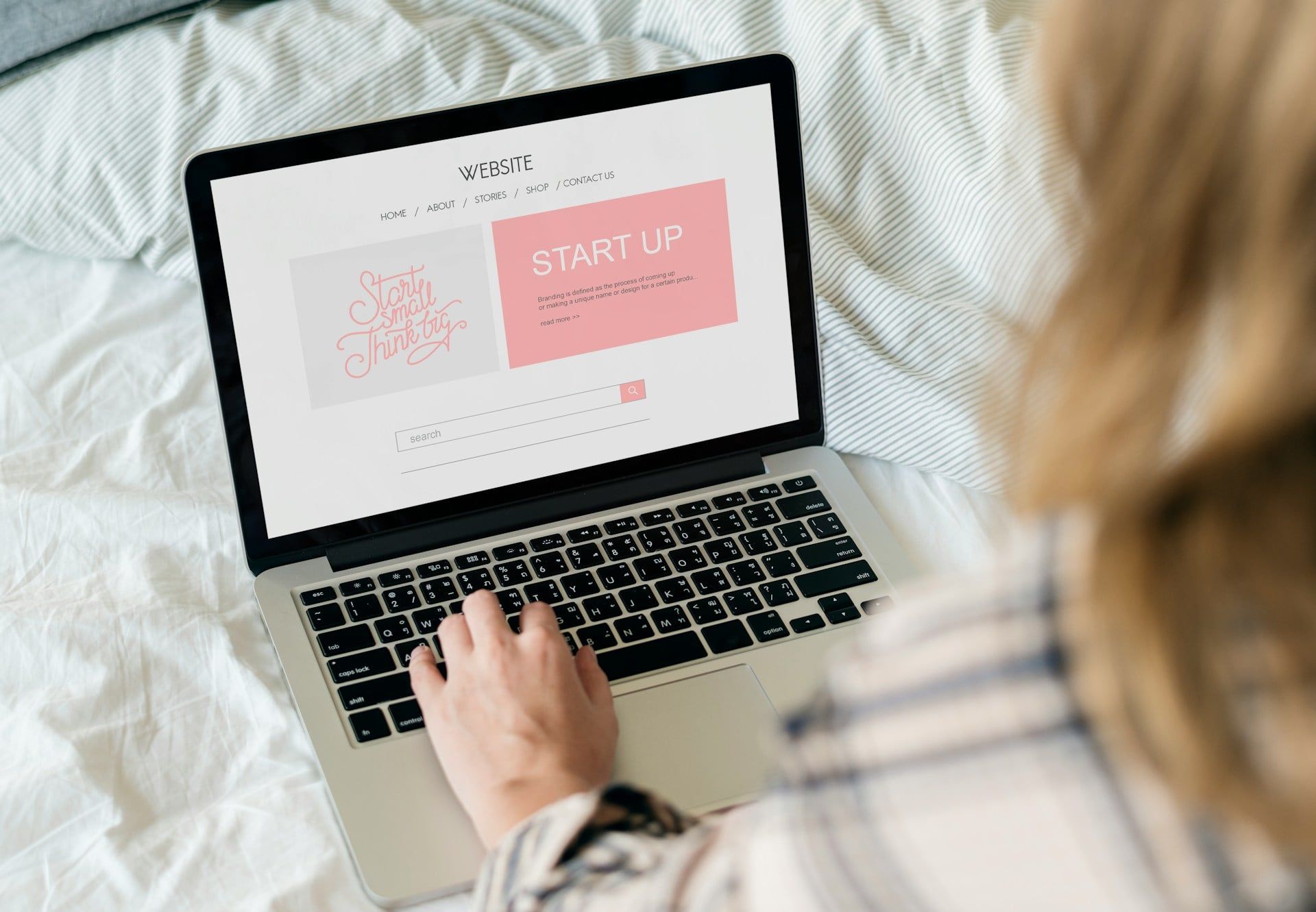 A woman sits in bed on her laptop, working on building her website