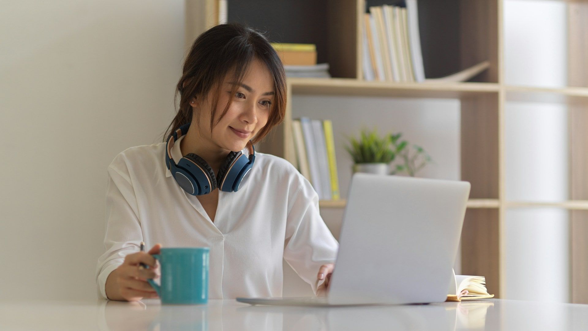 An Asian woman sits with a cup of coffee on her laptop looking for live chat solutions