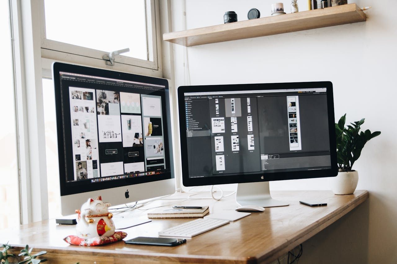 A wooden desk with two computer monitors displaying someone building their website