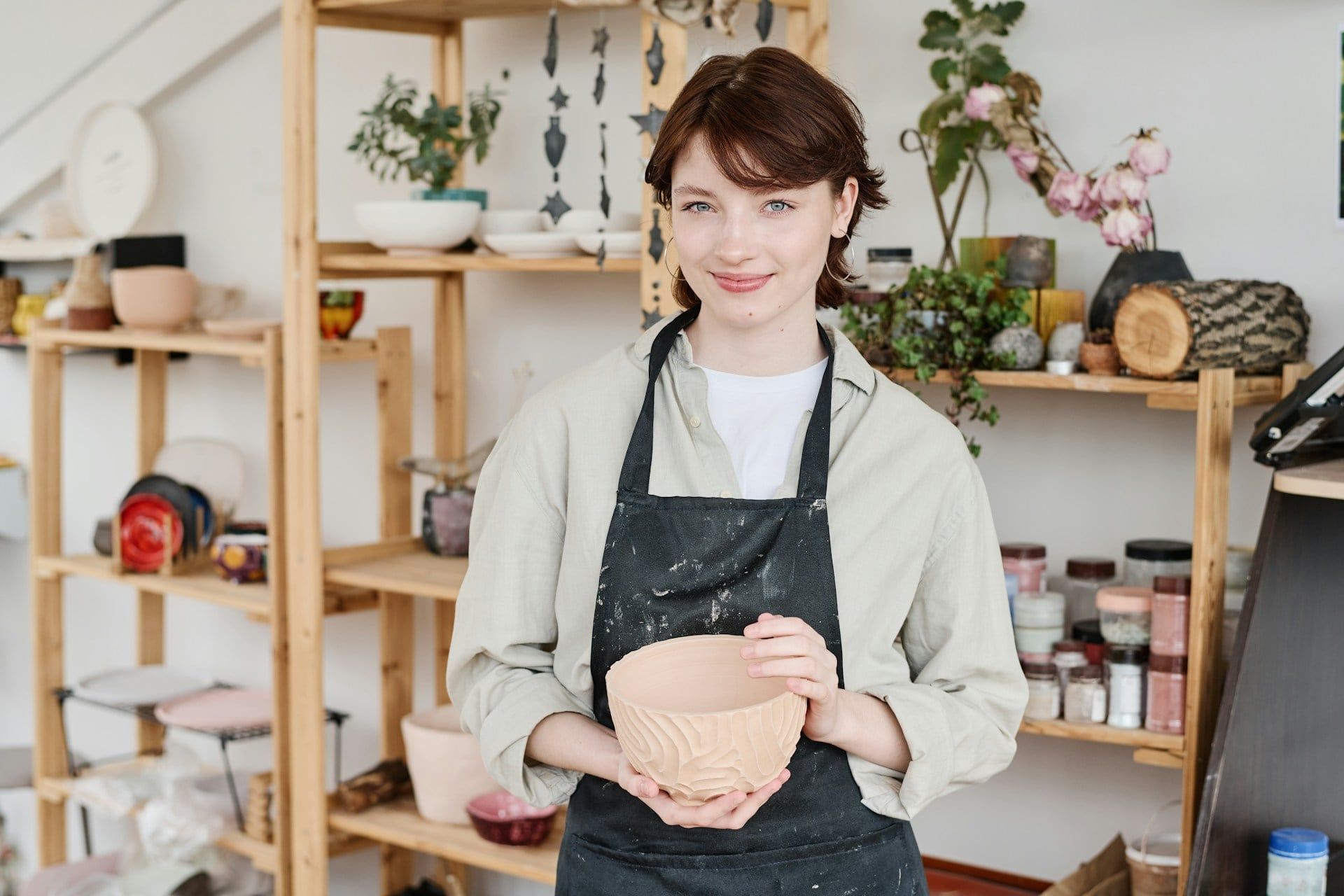 A small business owner smiles and poses with pottery from her business