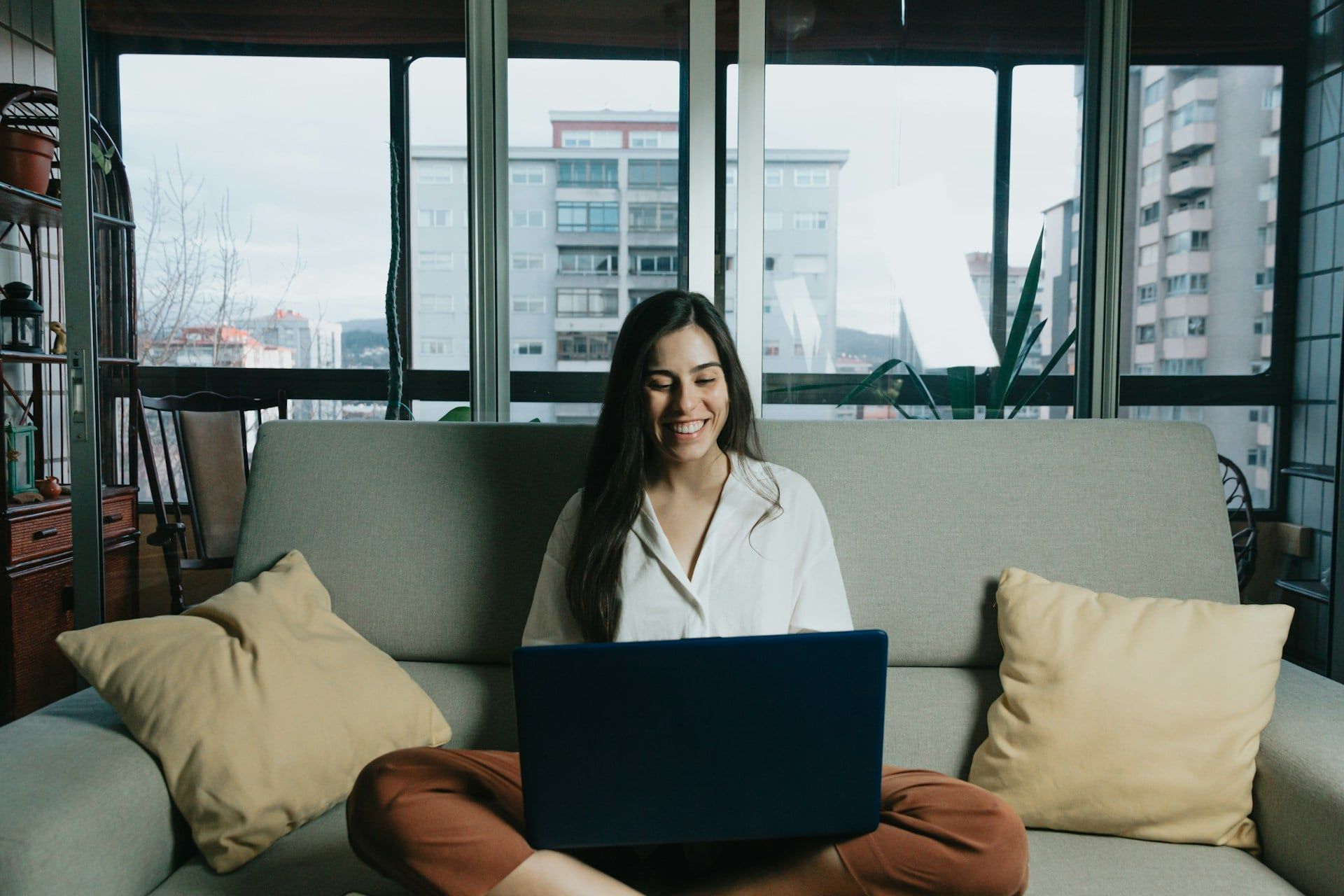 A female freelancer smiles while sitting cross-legged on a couch using her laptop