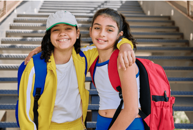 Two kids smiling and posing with each other upon their return to school after the summer
