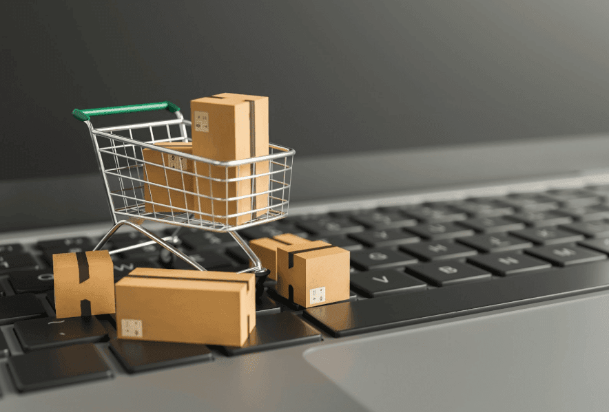 A laptop with toy boxes and a shopping cart on the keyboard representing e-Commerce and online shopping