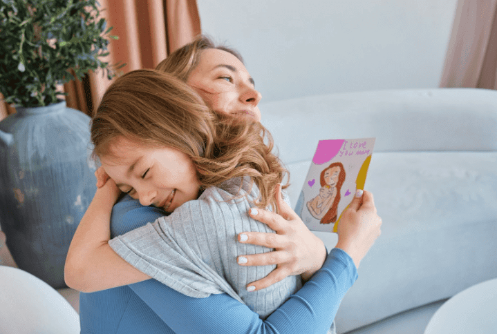 A mother and her daughter hugging on Mother’s Day with a handmade card