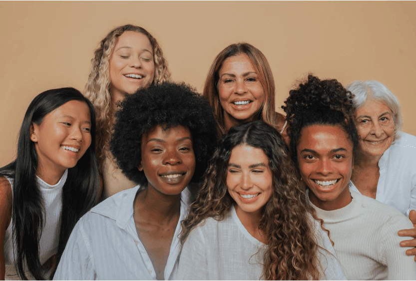 A group of women smile into the camera from all backgrounds on International Women’s Day