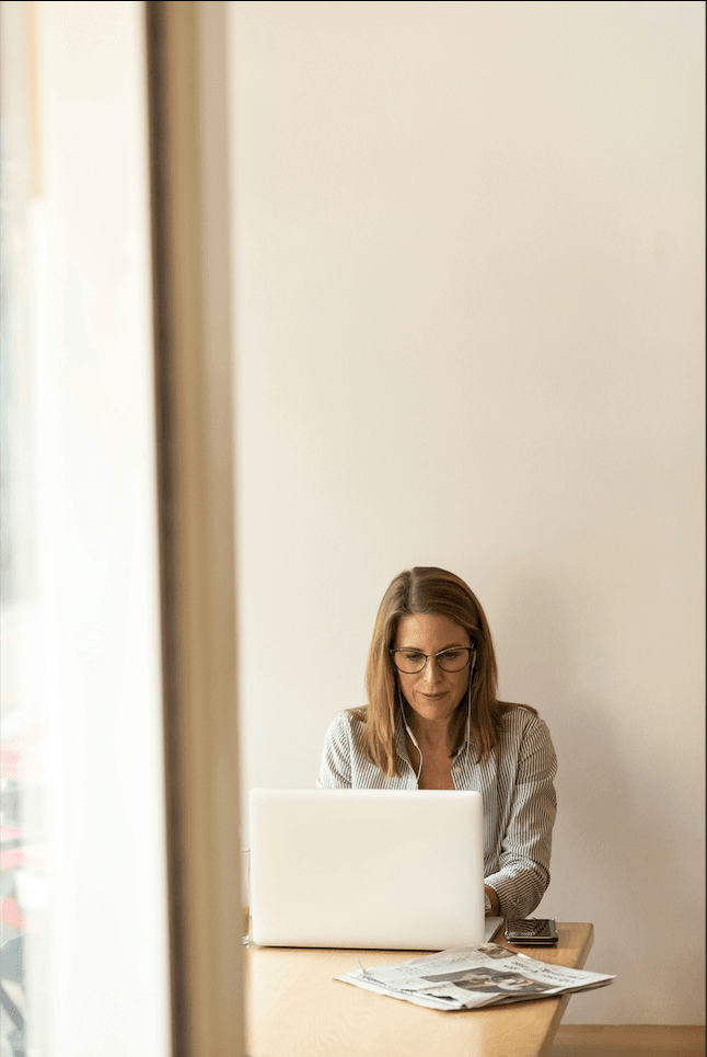 A girl sits at a coffee shop table, focused on her computer, with a warm and cozy atmosphere around her.