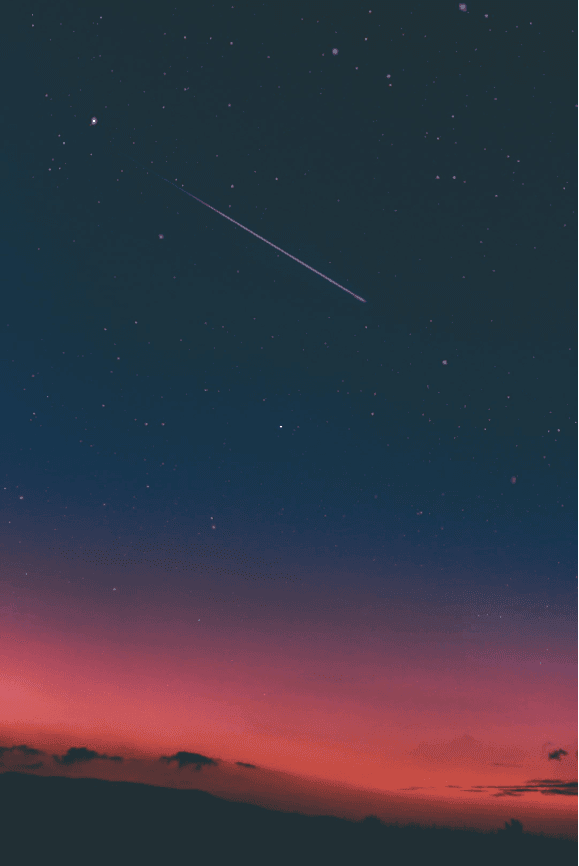 A brightly lit evening sky with a shooting star streaking across.