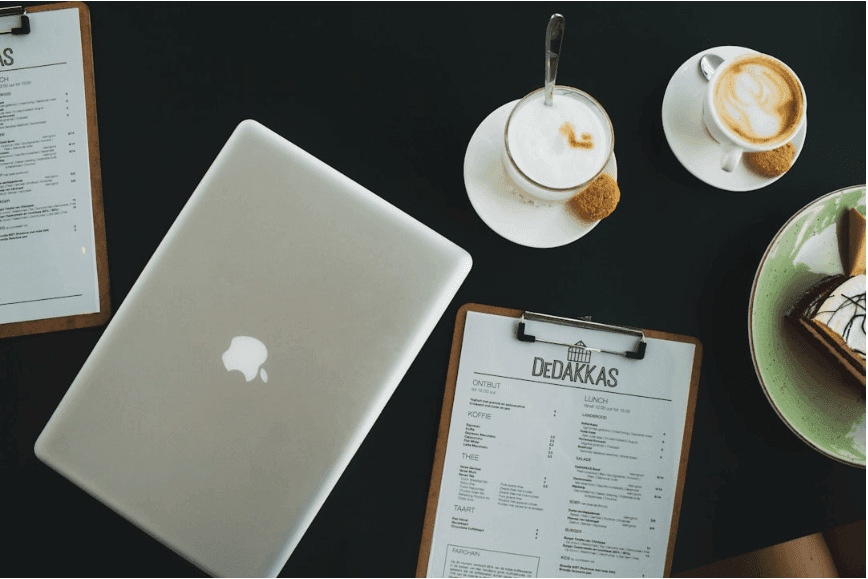 A laptop placed at a cafe table next to a cup of coffee and a menu.