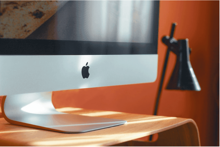 A desktop monitor placed on a wooden shelf, set against an orange wall.