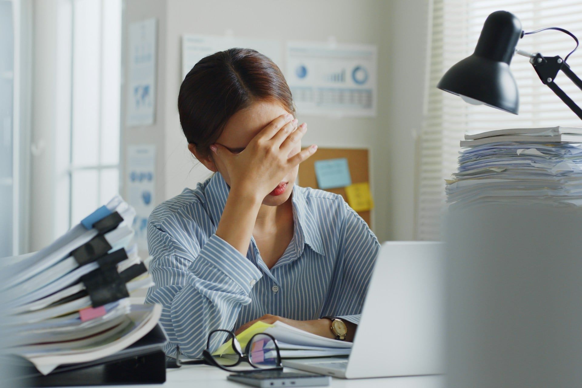 A female business owner sits at a desk looking stressed, surrounded by the challenge of paperwork