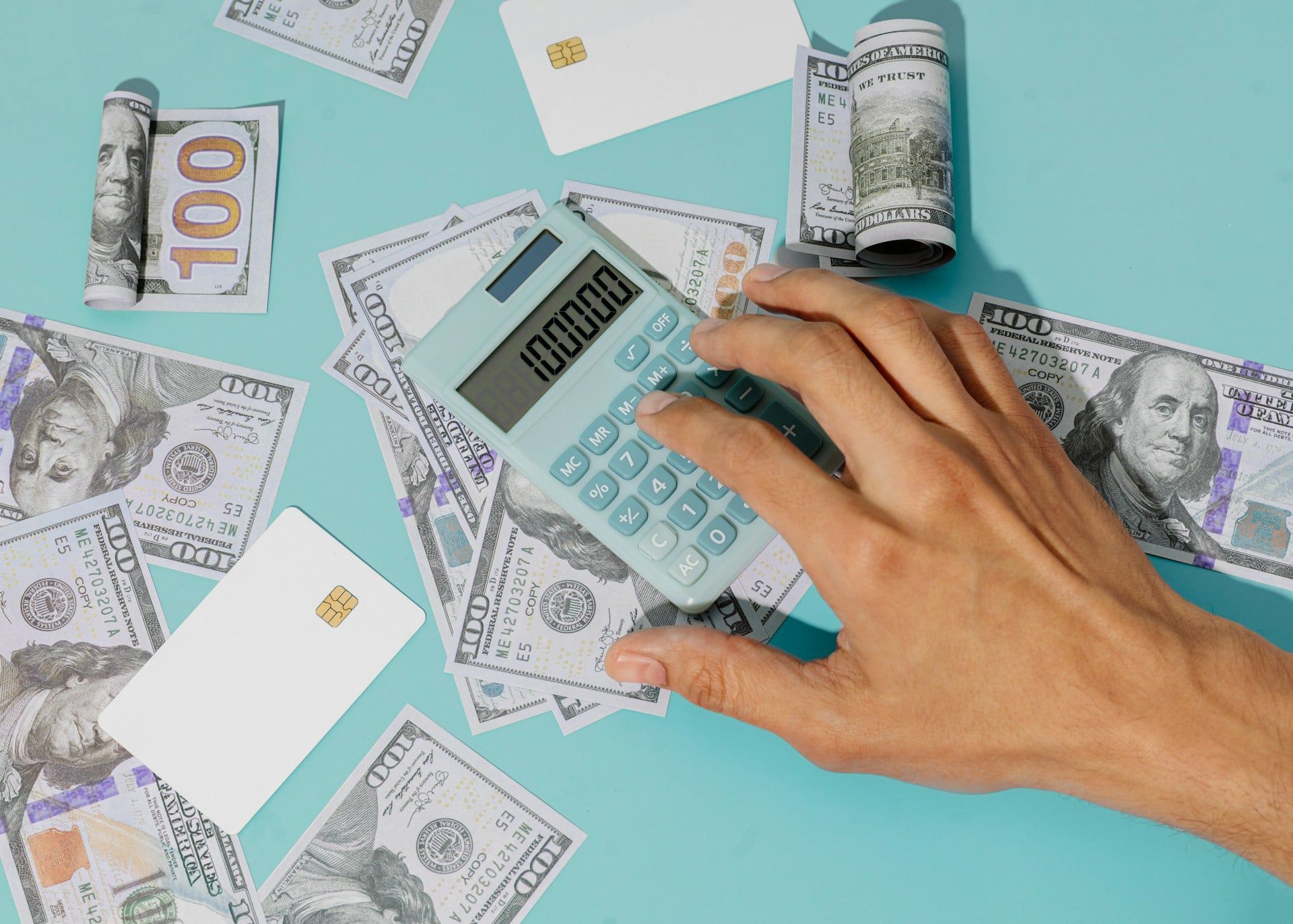 A blue background with lots of dollar bills and a hand using a calculator
