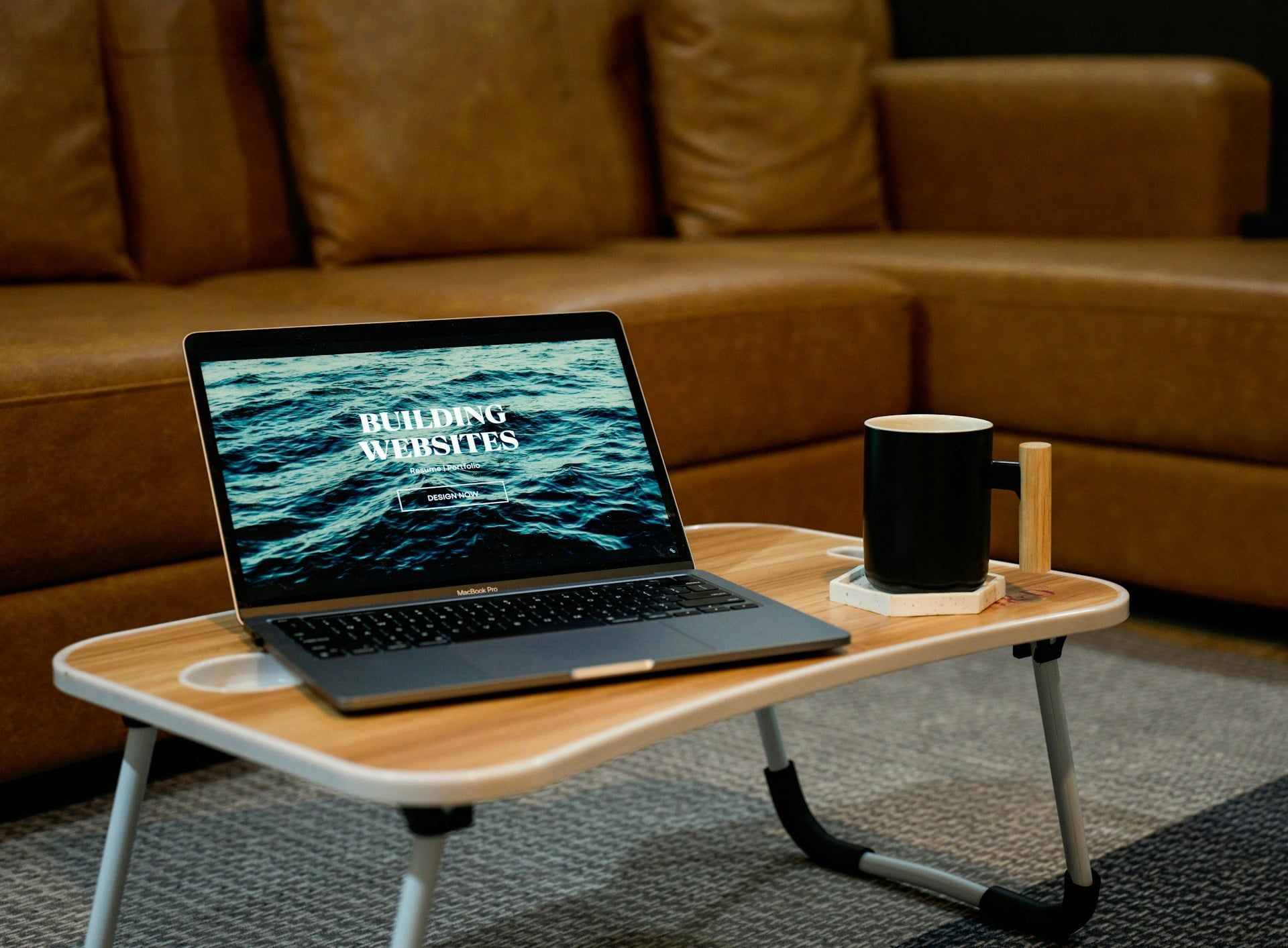 An open laptop on a coffee table with the words “Building Websites” on screen