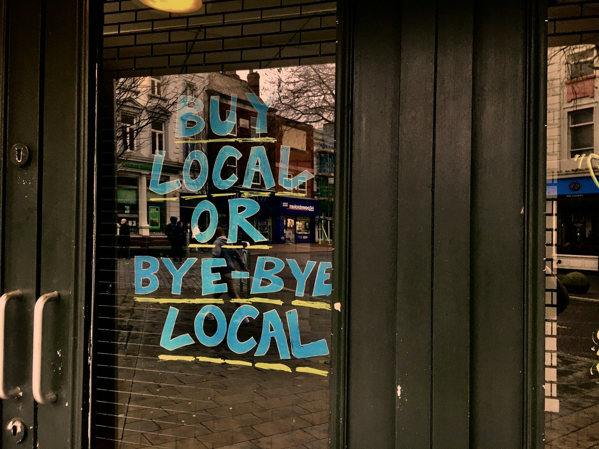 A local store with writing in the window that reads “Buy local or “bye bye local”