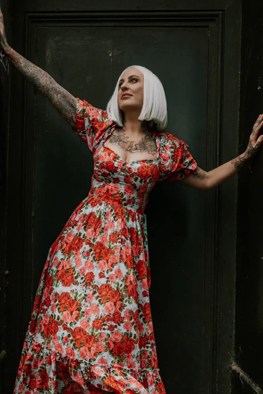 Expressive editorial model portrait in a red floral dress against a dark doorway