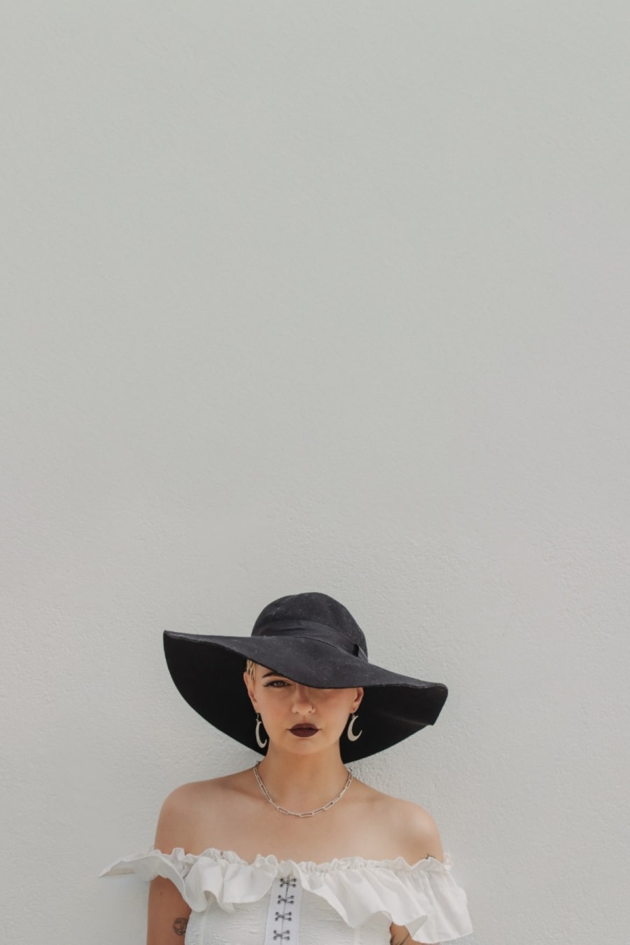 Minimalist fashion model portrait in a black wide-brimmed hat and white outfit