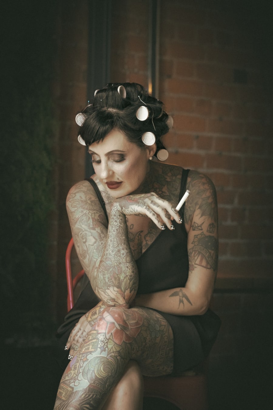 Atmospheric seated portrait of a tattooed woman with hair rollers