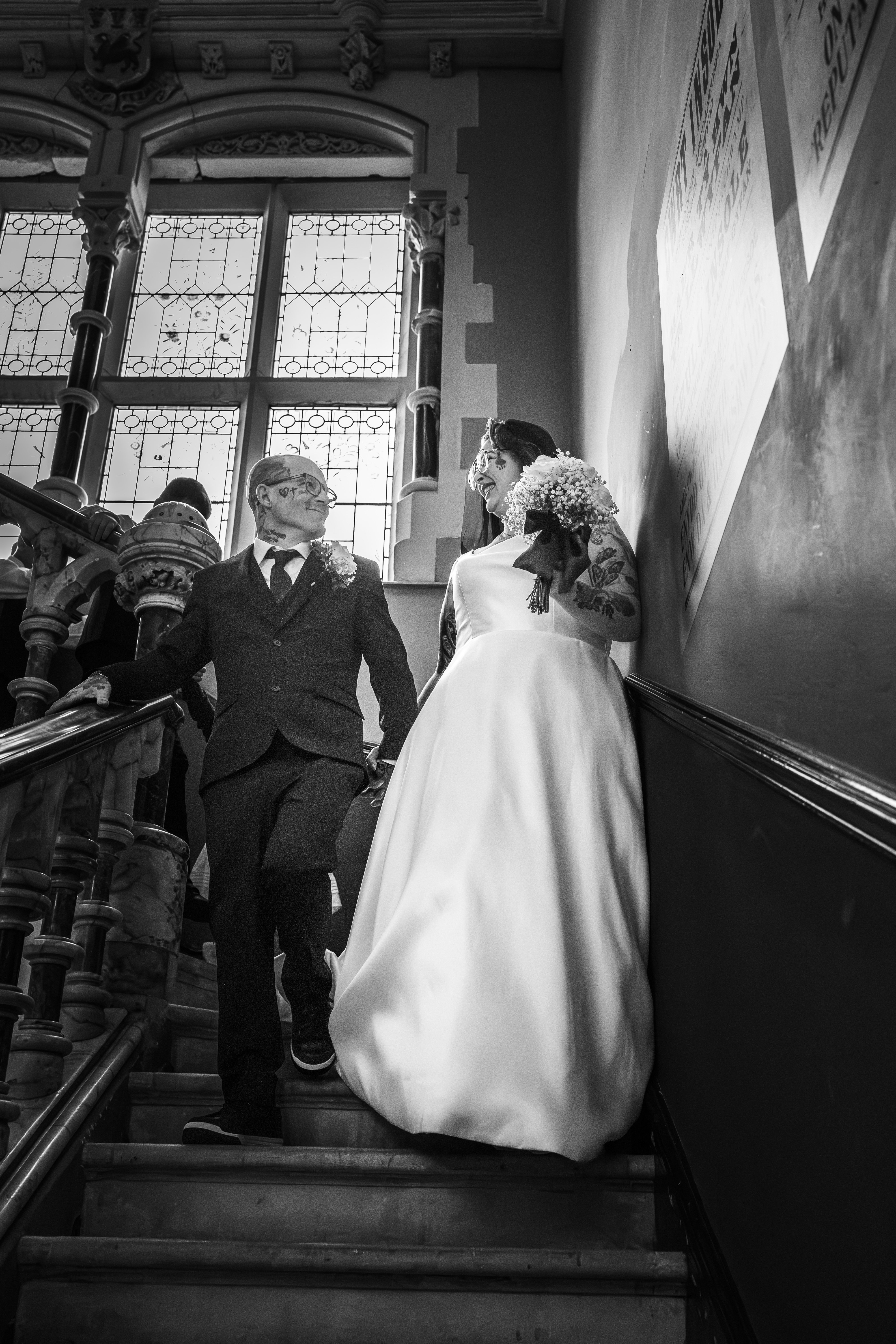 Couple laughing together on a staircase on their wedding day, photographed in black and white