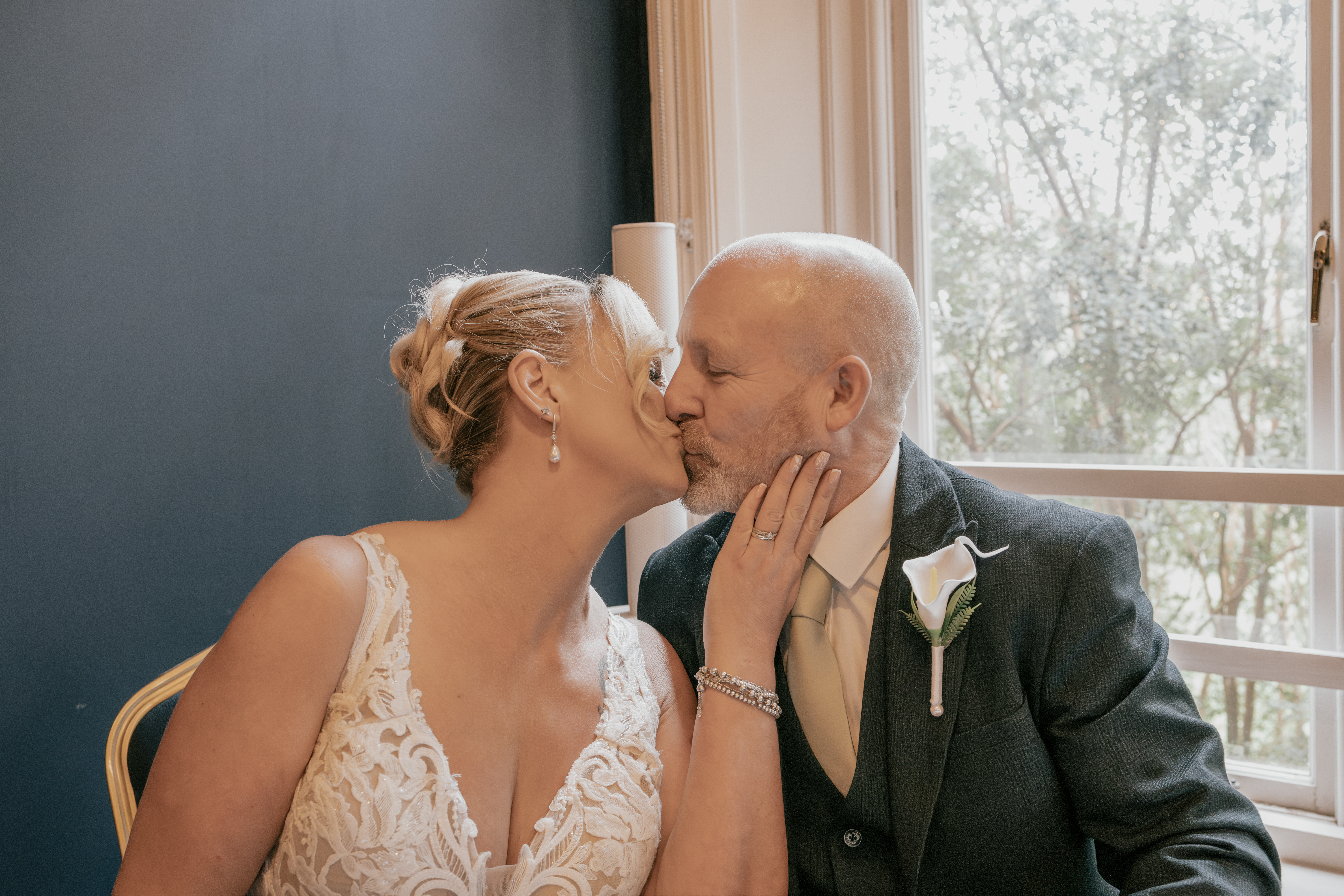 Newly married couple sharing an intimate kiss by a window