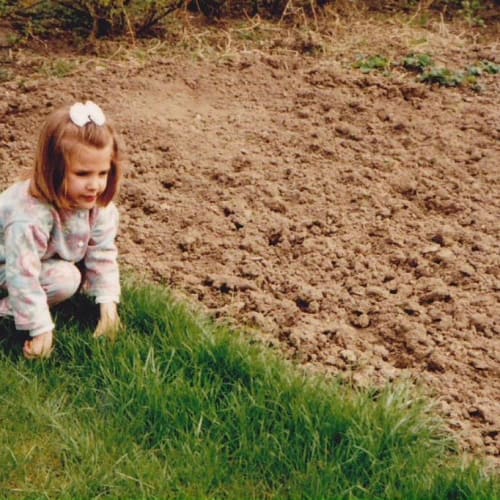Petite fille accroupie dans l'herbe à coté d'un terrain labouré