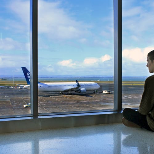 Femme de dos assise en tailleur au sol dans un aéroport de Nouvelle Zélande qui regarde un avion sur le tarmac